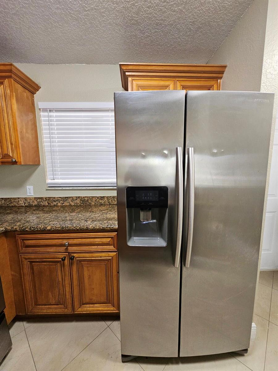 A stainless steel side-by-side refrigerator stands in a kitchen with wood cabinets and granite countertops — 1440 Windorah Way # C, West Palm Beach FL 33411, WEST PALM BEACH, FL