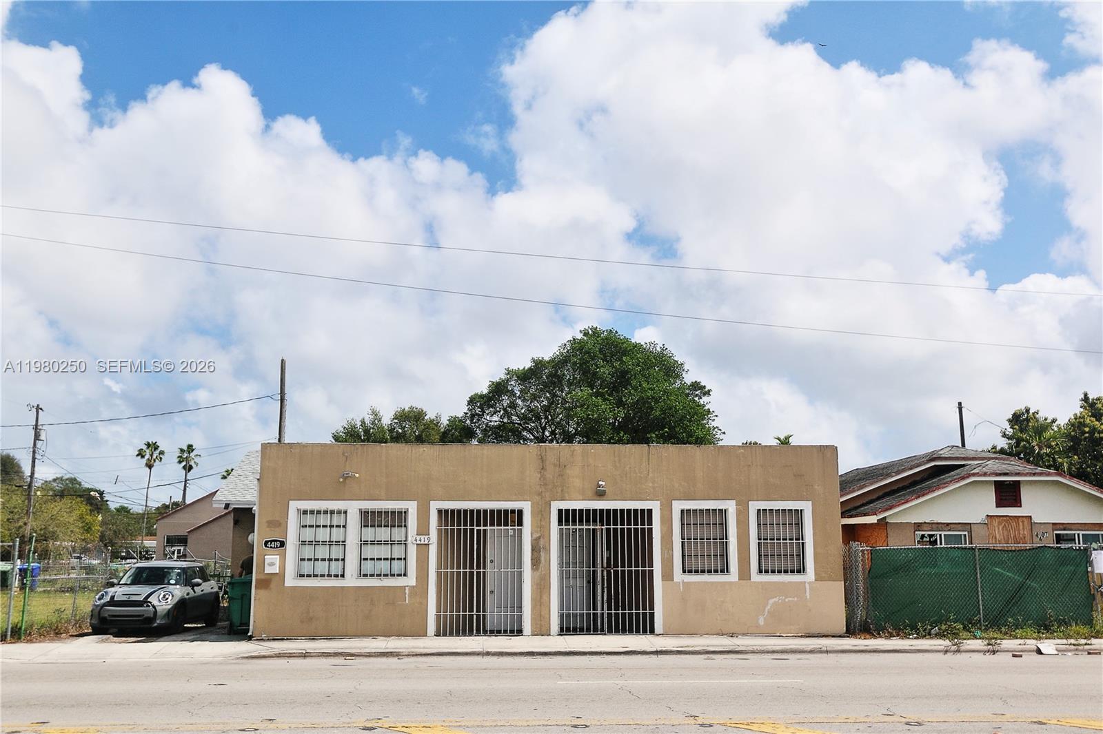A single-story tan commercial building with barred windows and doors sits beside a parked car — 4419 NW 17th Ave, Miami FL 33142, MIAMI, FL