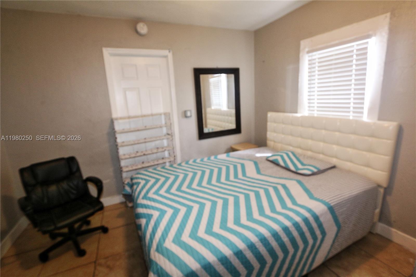 A bedroom features a bed with a chevron quilt, a black chair, and a mirror — 4419 NW 17th Ave, Miami FL 33142, MIAMI, FL