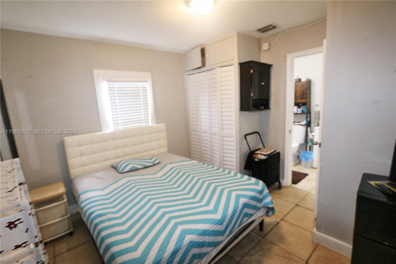 A bedroom features a bed with a chevron quilt, white louvered closets, and tiled floors — 4419 NW 17th Ave, Miami FL 33142, MIAMI, FL