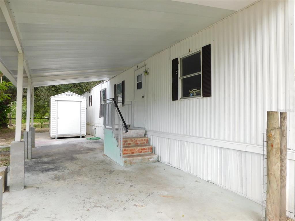 A white mobile home exterior features a covered carport, concrete pad, and a small storage shed — 1110 NE FORREST AVENUE, ARCADIA, FL