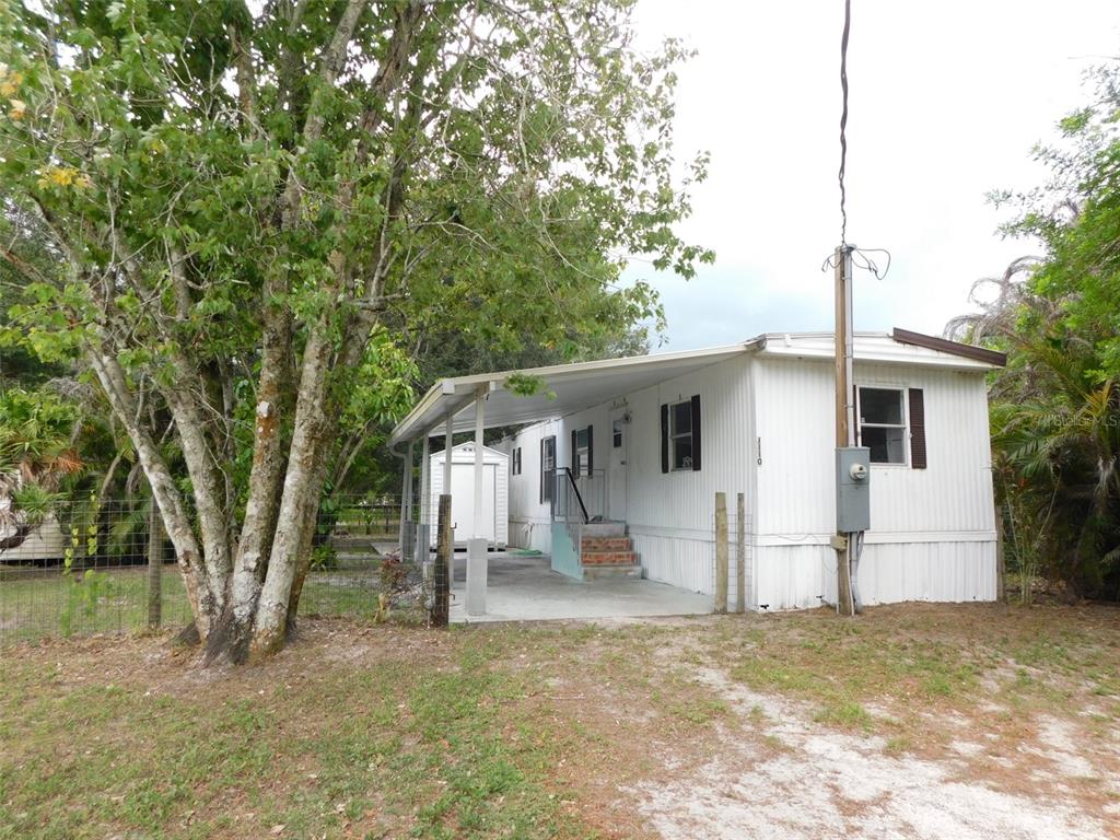A white mobile home with a carport and a small shed stands near large trees — 1110 NE FORREST AVENUE, ARCADIA, FL