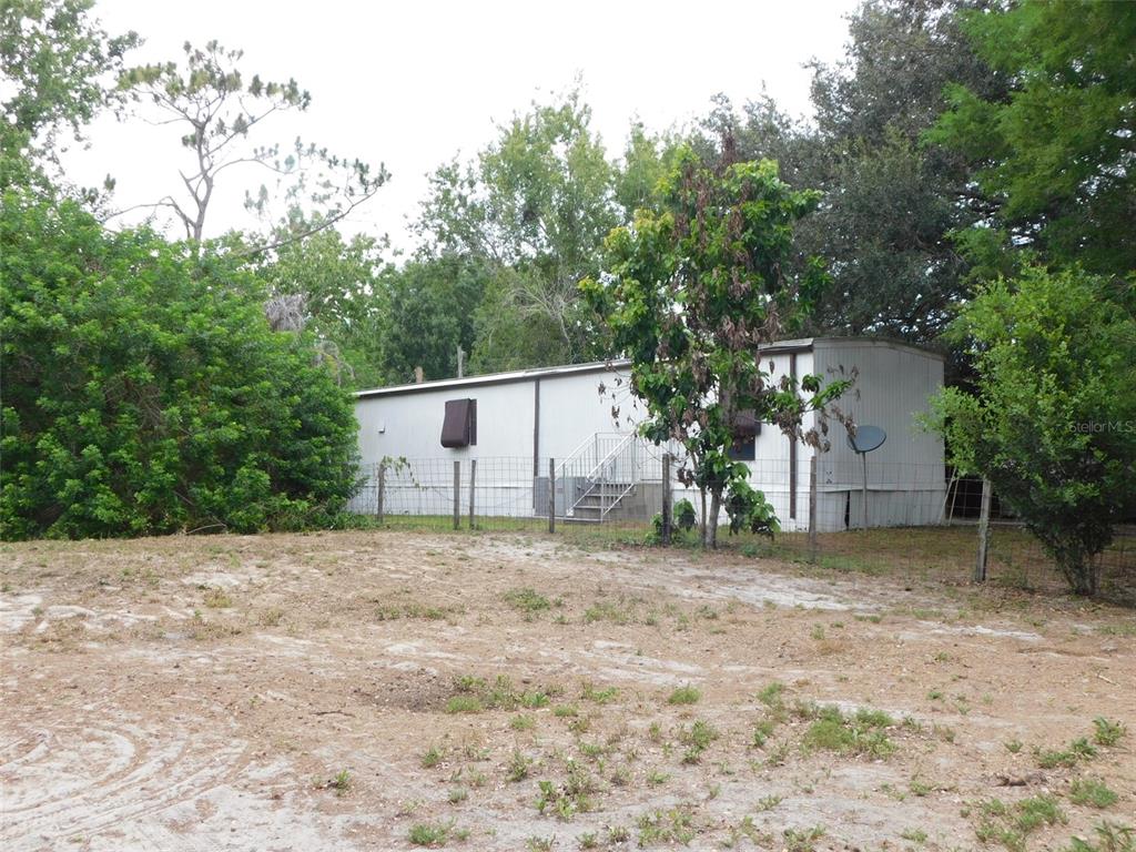 A single-story mobile home sits behind a wire fence on a sandy lot — 1110 NE FORREST AVENUE, ARCADIA, FL