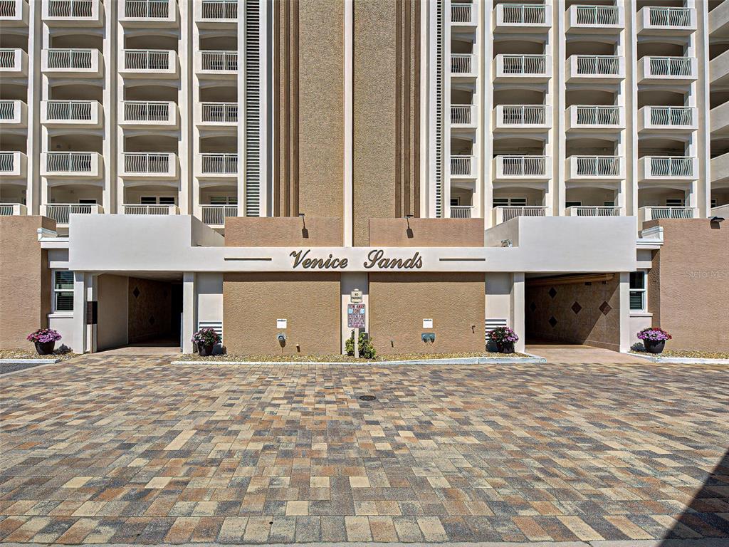 The exterior of the Venice Sands condominium building features a paved driveway and covered parking — 633 ALHAMBRA ROAD UNIT 1006, VENICE, FL