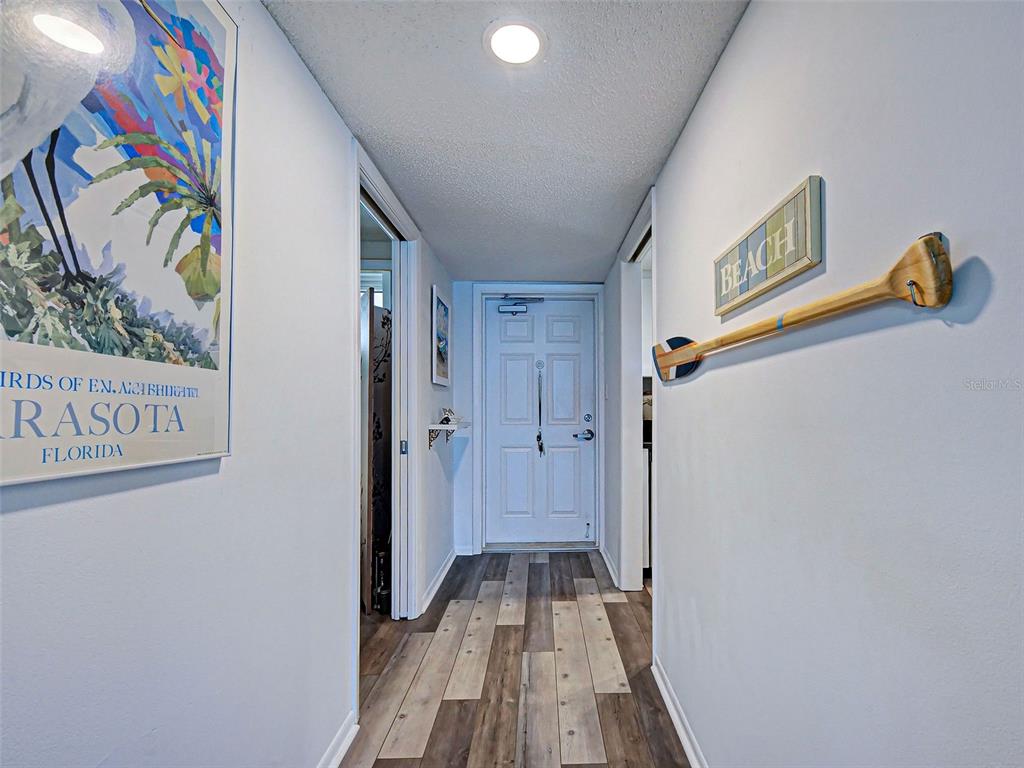 A hallway features wood-look flooring, a white front door, and wall-mounted beach-themed decor — 633 ALHAMBRA ROAD UNIT 1006, VENICE, FL