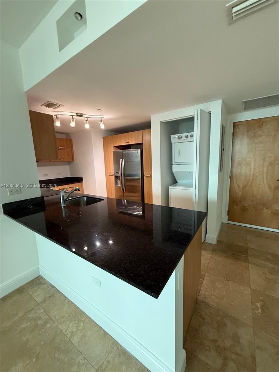 A kitchen features a black granite countertop, stainless steel refrigerator, and a stacked laundry unit — 350 S Miami Ave # 2603, Miami FL 33130, MIAMI, FL