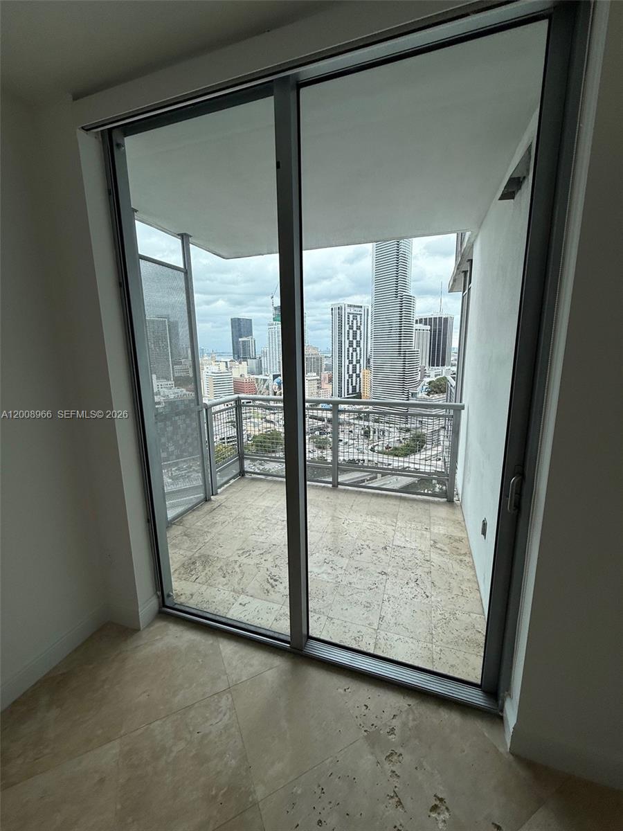 A balcony with stone flooring overlooks a city skyline through large sliding glass doors — 350 S Miami Ave # 2603, Miami FL 33130, MIAMI, FL