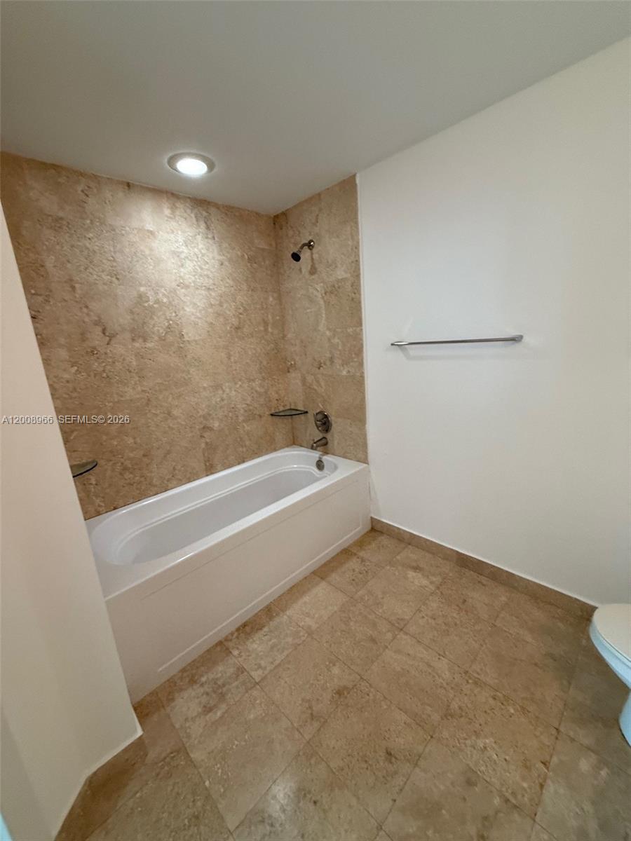 A bathroom features a white bathtub with tan stone tile walls and matching floor tiles — 350 S Miami Ave # 2603, Miami FL 33130, MIAMI, FL
