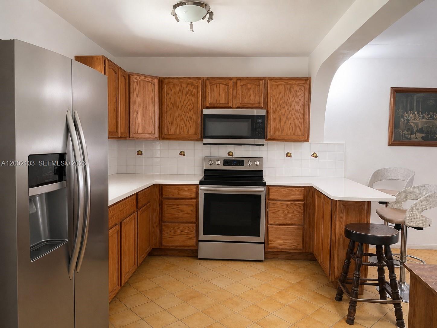 A kitchen features oak cabinets, stainless steel appliances, white countertops, and light-colored tile flooring — 10820 NE 5th Ave, Miami FL 33161, MIAMI, FL