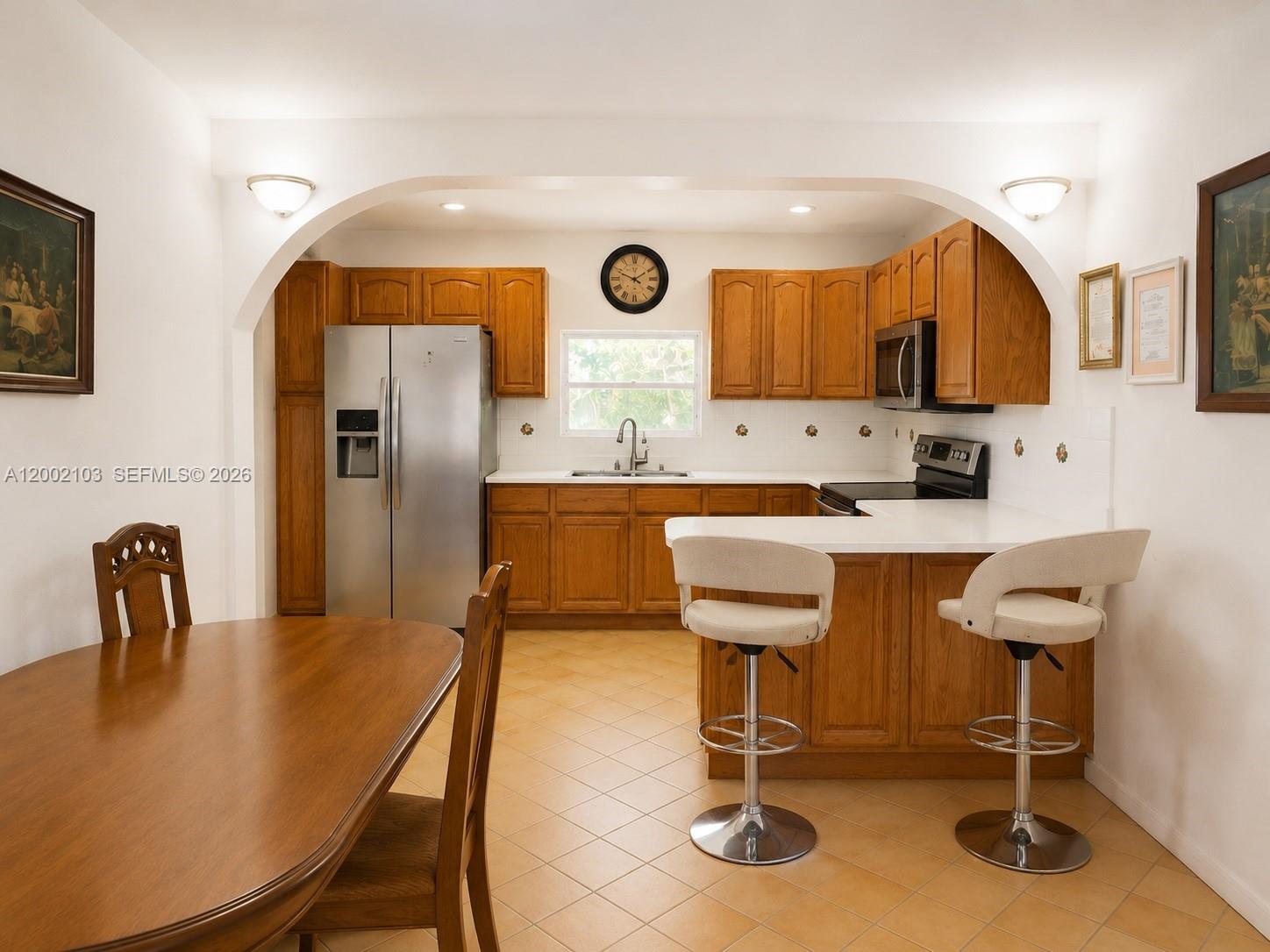 A kitchen with wood cabinets, stainless steel appliances, and a breakfast bar with two stools — 10820 NE 5th Ave, Miami FL 33161, MIAMI, FL