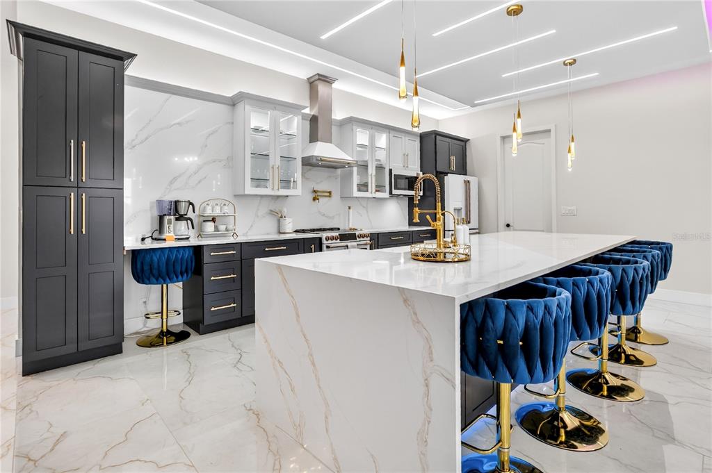 A modern kitchen features a large marble island, blue velvet stools, and dark cabinetry — 18965 SHELDON STREET, ORLANDO, FL