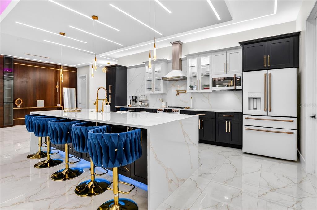 A modern kitchen features a large marble-topped island, blue velvet barstools, and two-toned cabinetry — 18965 SHELDON STREET, ORLANDO, FL