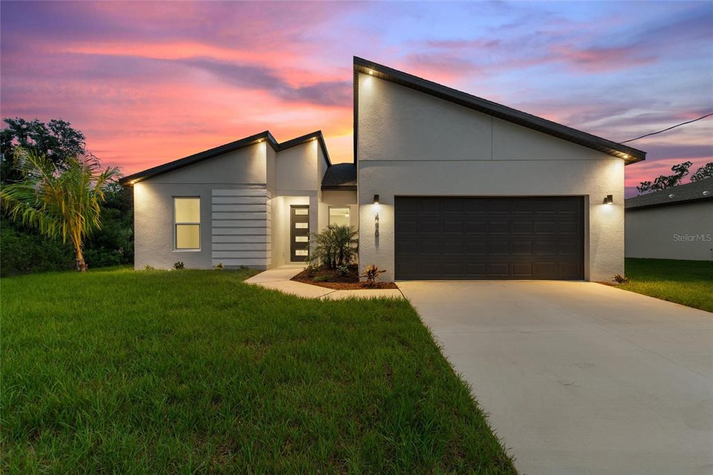 A modern single-story house with a two-car garage and a sunset sky background — 4709 FLINT DRIVE, NORTH PORT, FL