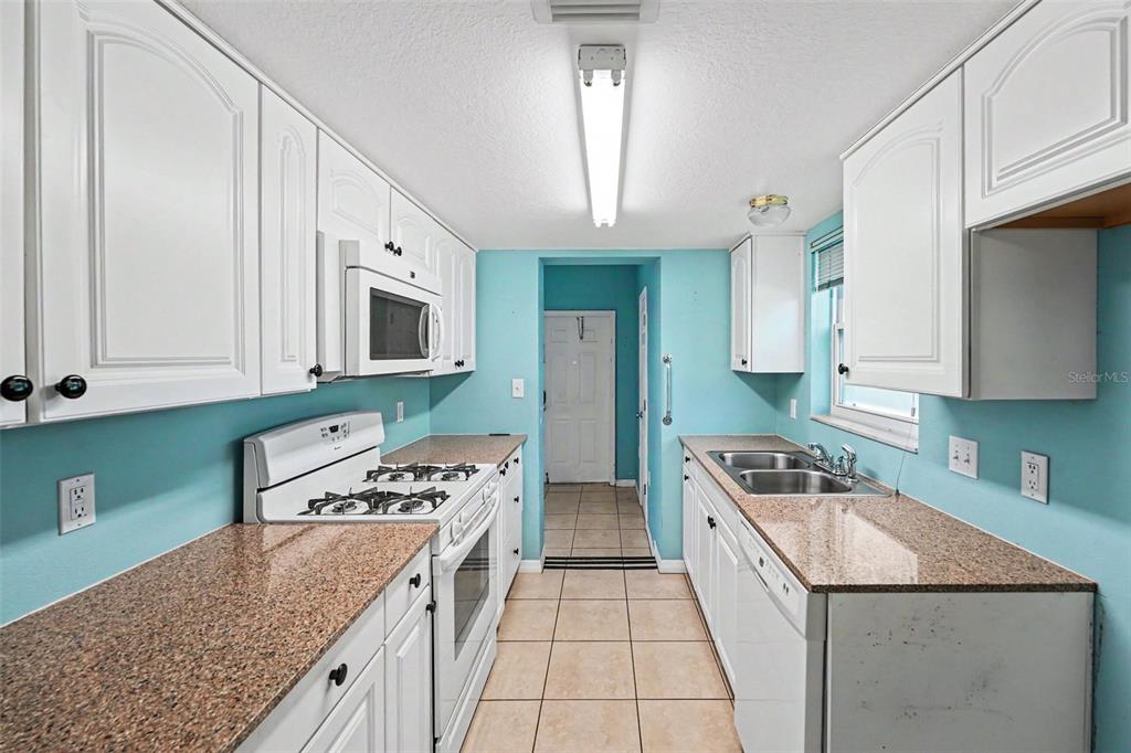 A galley kitchen features white cabinets, granite countertops, light blue walls, and tile flooring — 5855 18TH STREET N UNIT 1, ST PETERSBURG, FL