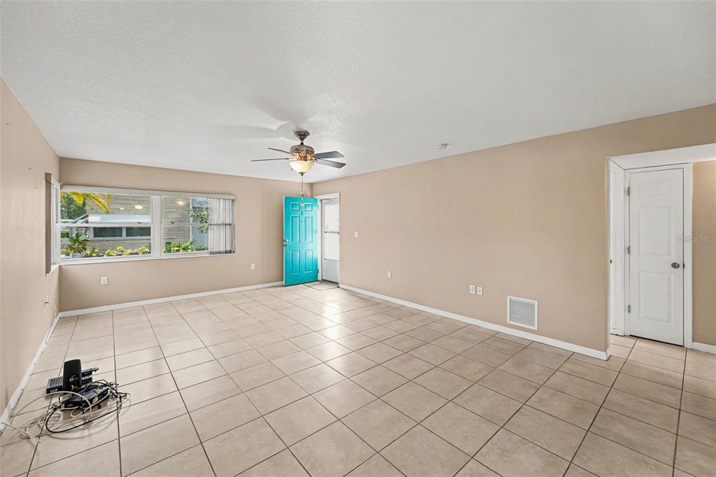 A living room with beige walls, light-colored tile flooring, a ceiling fan, and a turquoise door — 5855 18TH STREET N UNIT 1, ST PETERSBURG, FL