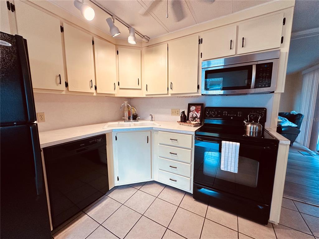 A kitchen features white cabinets, black appliances, a corner sink, and tiled flooring — 1100 BELCHER ROAD S UNIT 185, LARGO, FL