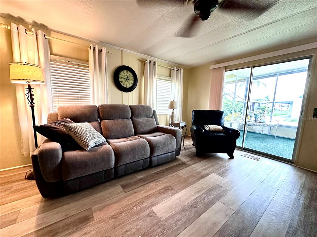 A living room features a gray sofa, a black armchair, and wood-look flooring — 1100 BELCHER ROAD S UNIT 185, LARGO, FL