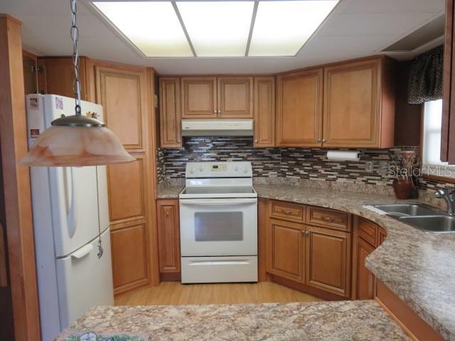 A kitchen features light wood cabinets, a white stove, and a patterned tile backsplash — 2107 PALMA SOLA BOULEVARD UNIT 8, BRADENTON, FL