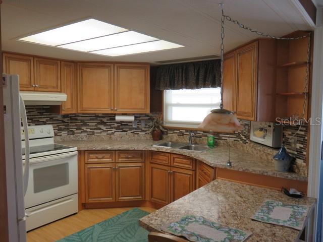 A kitchen with wood cabinets, granite countertops, a tiled backsplash, and a white stove — 2107 PALMA SOLA BOULEVARD UNIT 8, BRADENTON, FL