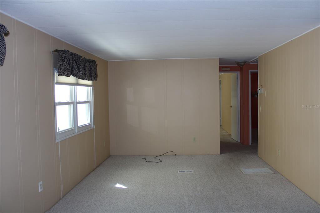 An empty room with tan paneled walls, beige carpeting, and a window with patterned valances — 2107 PALMA SOLA BOULEVARD UNIT 8, BRADENTON, FL
