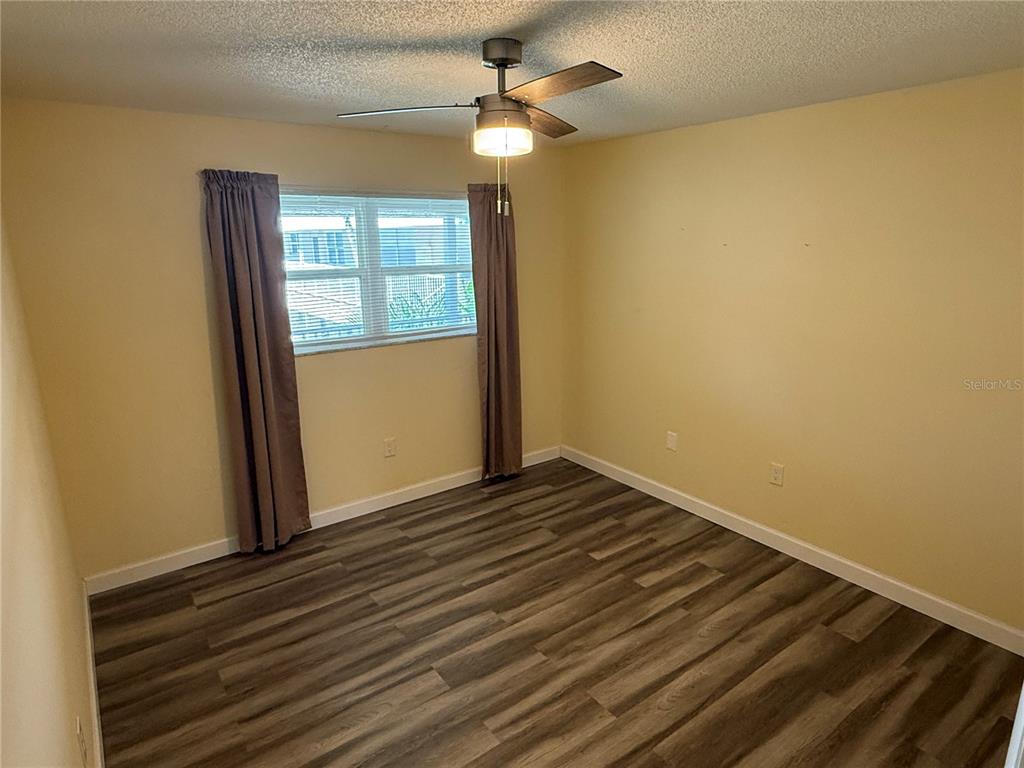 An empty bedroom features light yellow walls, wood-look flooring, and a ceiling fan — 10038 62ND TERRACE N UNIT 23, SEMINOLE, FL
