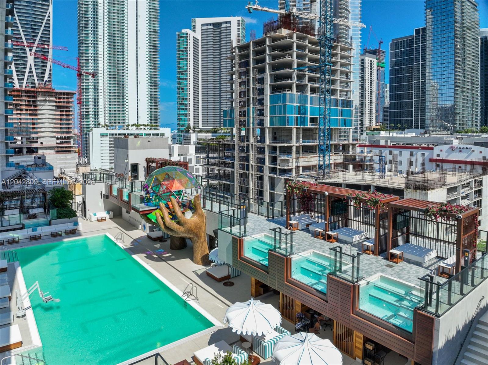 An outdoor pool deck features a large hand sculpture holding a colorful geometric sphere — 20 NE 11 # 2410, Miami FL 33132, MIAMI, FL