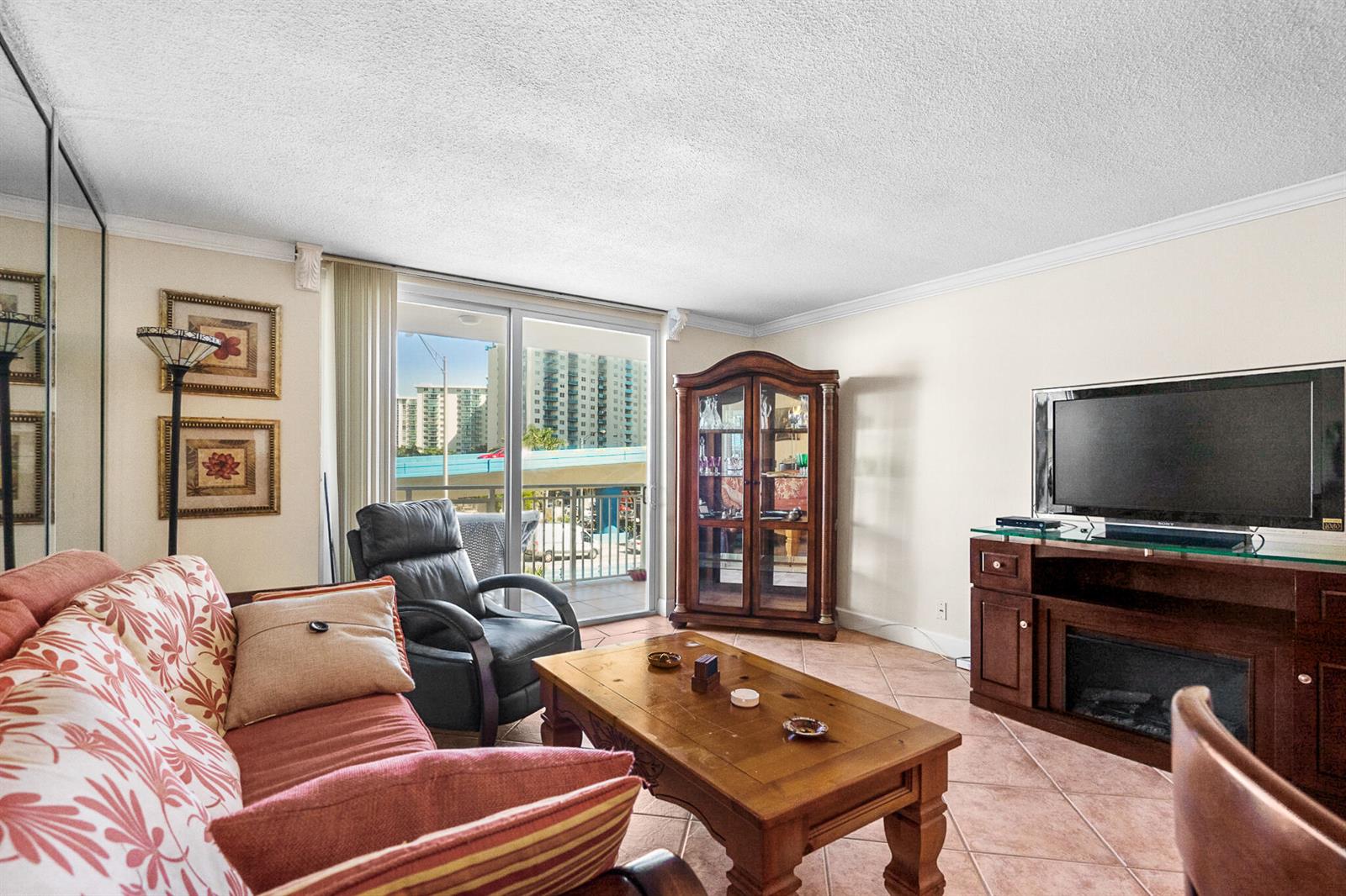 A living room with tile floors, a sofa, a coffee table, and a balcony view — 1801 S Ocean Drive Unit 332, Hallandale Beach FL 33009, HALLANDALE BEACH, FL