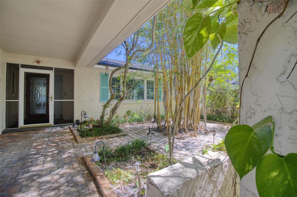 A paved courtyard features a bamboo grove, garden beds, and a covered entryway with doors — 2972 KENILWICK DRIVE S, CLEARWATER, FL
