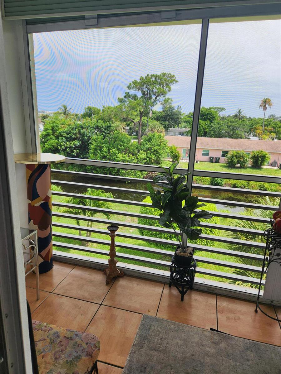 A screened-in balcony with tile flooring overlooks a canal, green trees, and a neighboring building — 2606 Garden Drive # 304, FL 33461, FL