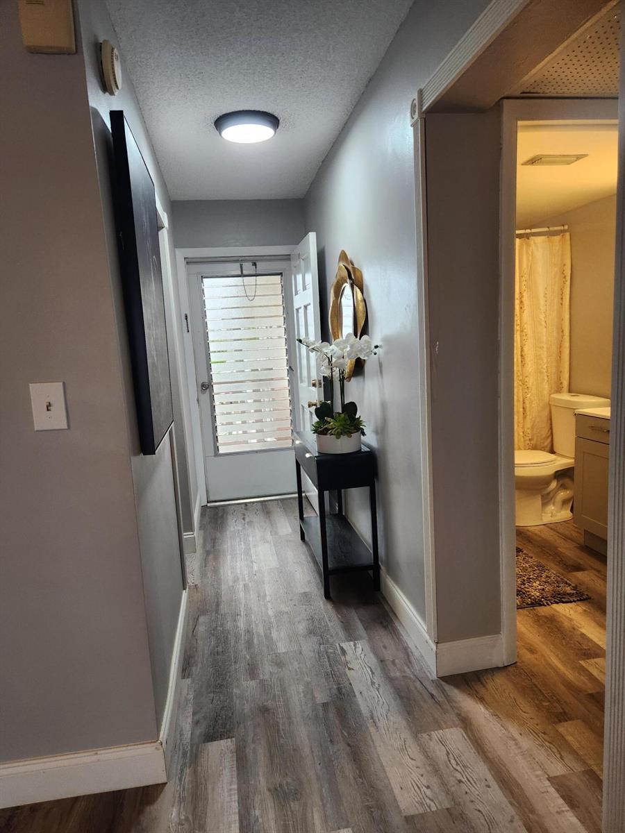 A hallway with gray walls, wood-look flooring, a console table, and an adjacent bathroom — 2606 Garden Drive # 304, FL 33461, FL