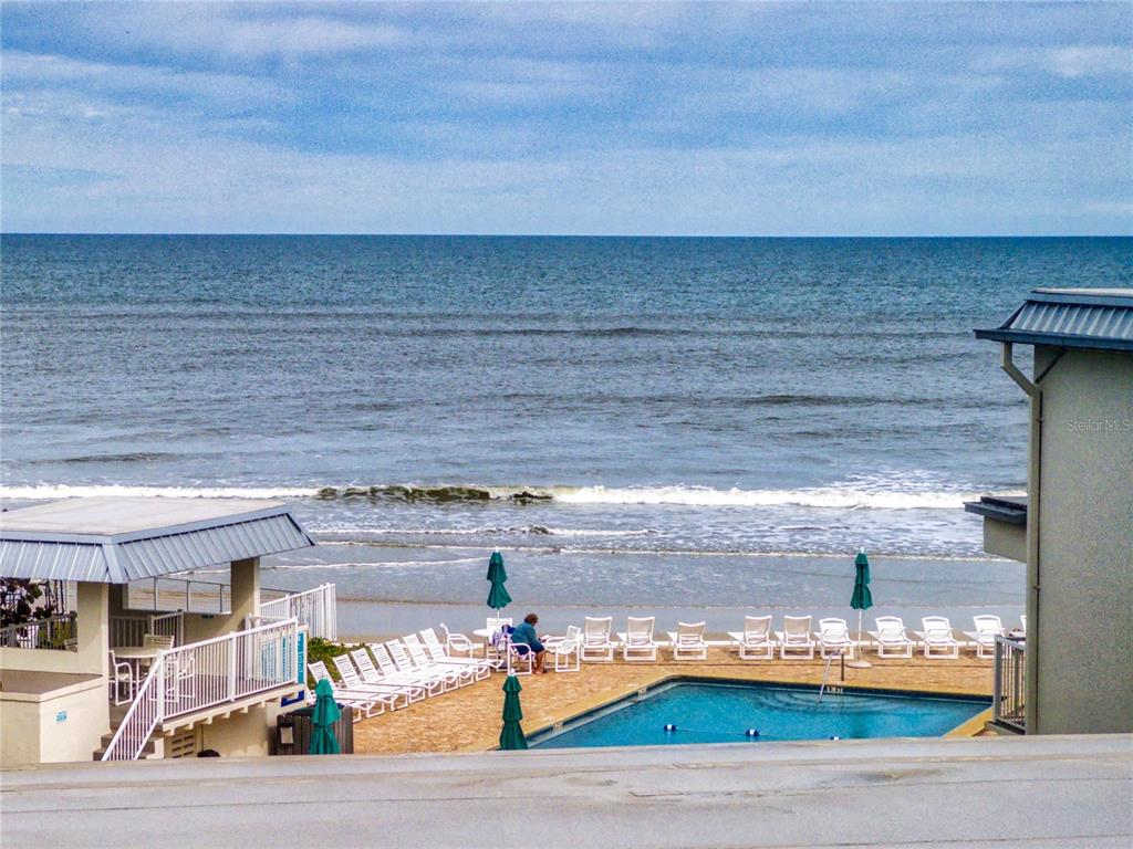 An elevated view of a beachside swimming pool with lounge chairs and ocean waves — 4849 SAXON DRIVE UNIT C208, NEW SMYRNA BEACH, FL