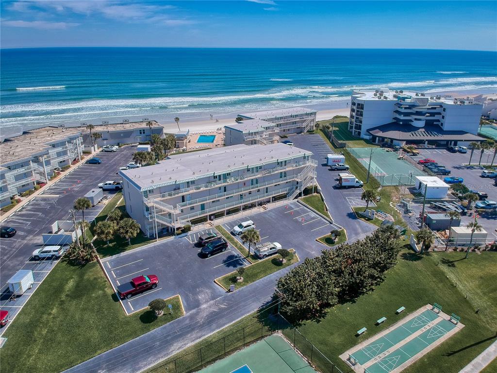 An aerial view shows a multi-story apartment building with a parking lot near the beach — 4849 SAXON DRIVE UNIT C208, NEW SMYRNA BEACH, FL