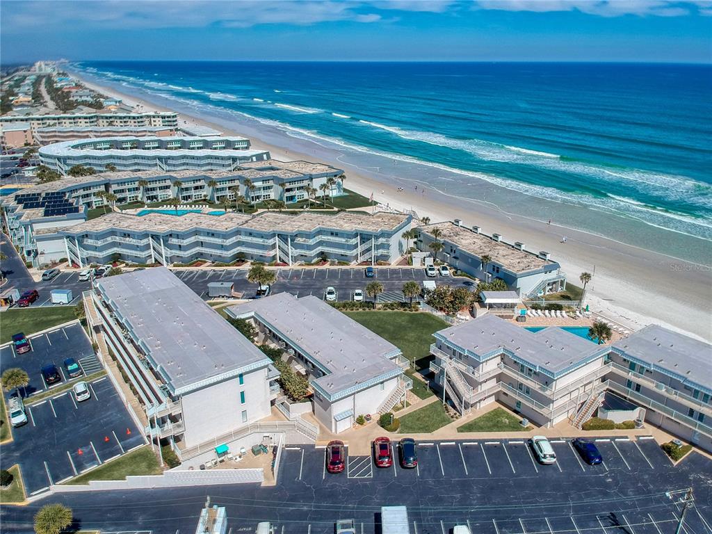 An aerial view shows a multi-story beachfront condominium complex with parking lots and a pool — 4849 SAXON DRIVE UNIT C208, NEW SMYRNA BEACH, FL