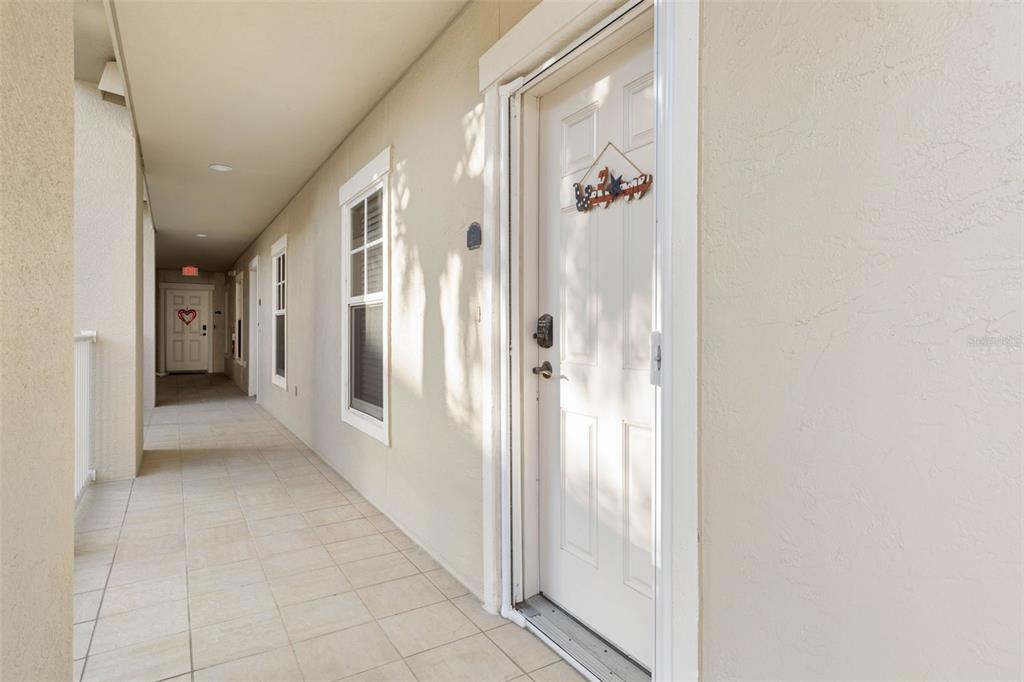 A tiled outdoor walkway leads to a white front door with a decorative hanging sign — 146 PALM COAST RESORT BOULEVARD UNIT 203, PALM COAST, FL