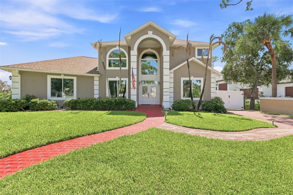 A two-story house with a beige stucco exterior, arched entryway, and red brick walkway — 2340 NEWFOUND HARBOR DRIVE, MERRITT ISLAND, FL