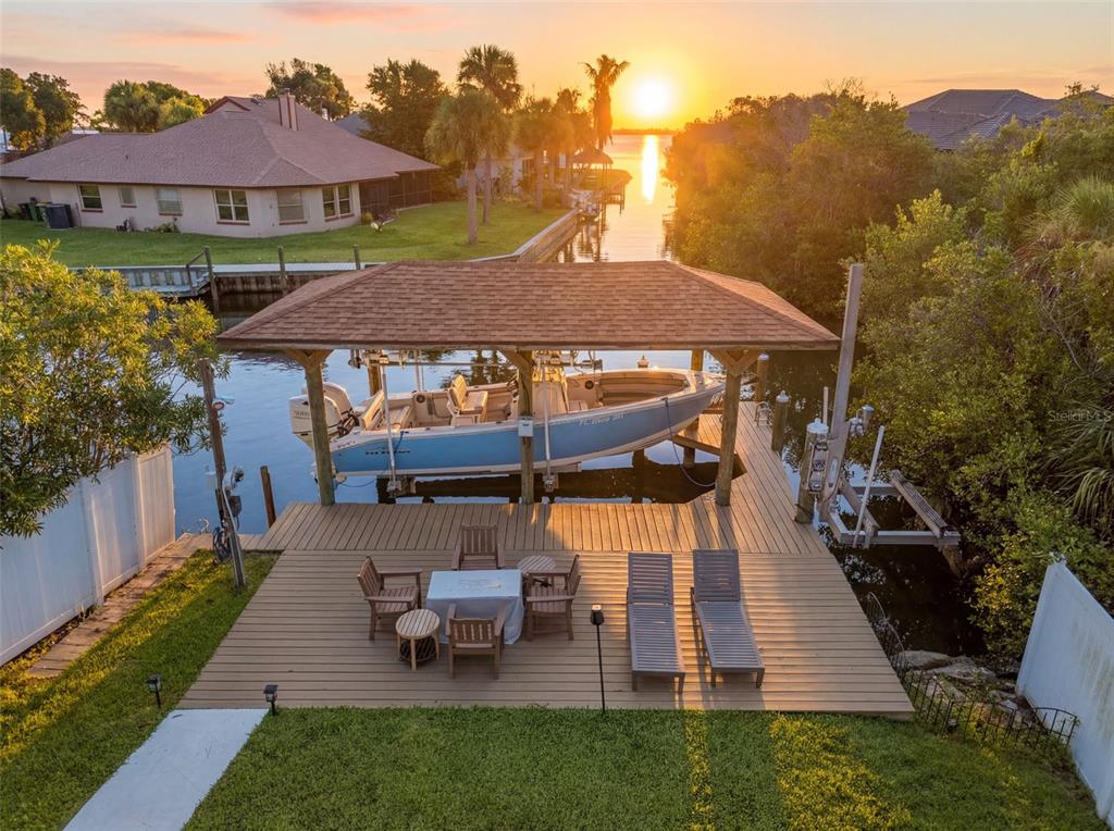 An aerial view of a wooden dock with a boat lift, seating area, and sunset — 2340 NEWFOUND HARBOR DRIVE, MERRITT ISLAND, FL