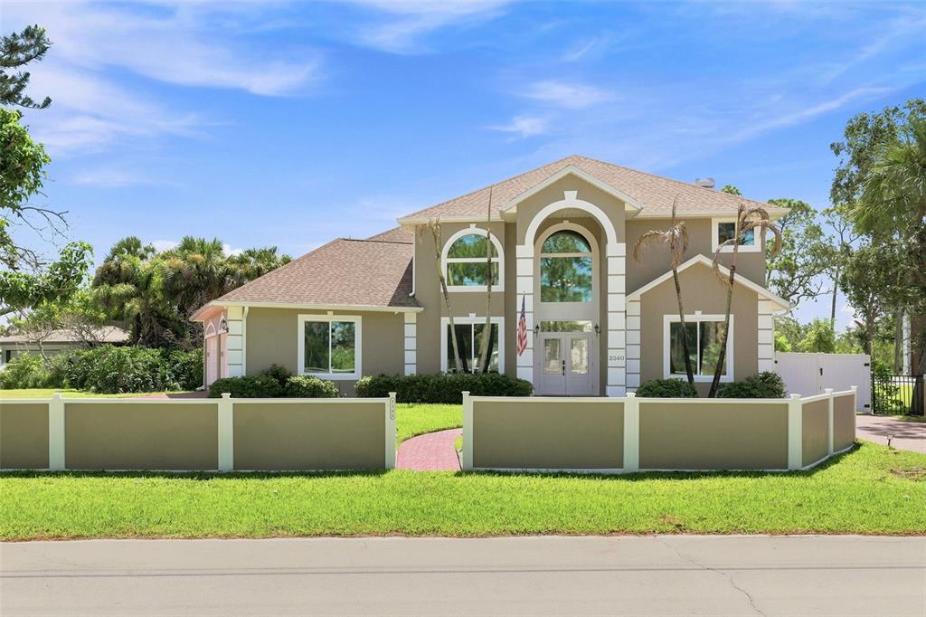 A two-story house with a tan exterior and a front yard enclosed by a fence — 2340 NEWFOUND HARBOR DRIVE, MERRITT ISLAND, FL