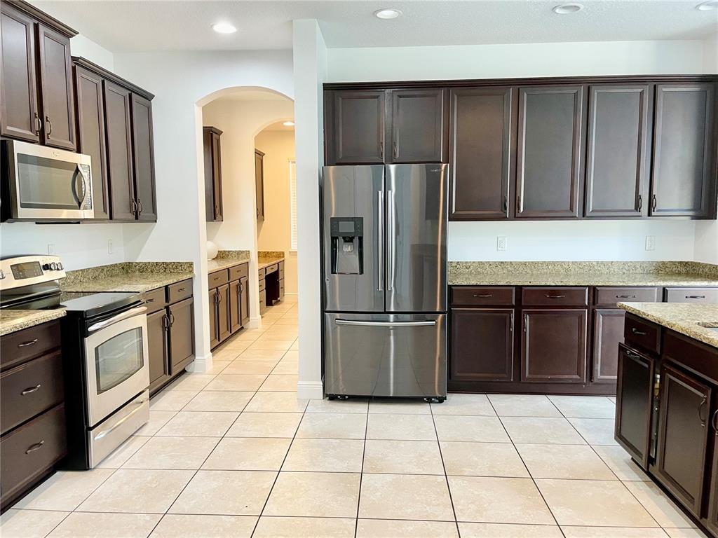 A kitchen features dark wood cabinets, granite countertops, stainless steel appliances, and light tile flooring — 7952 HAMPTON LAKE DRIVE, TAMPA, FL