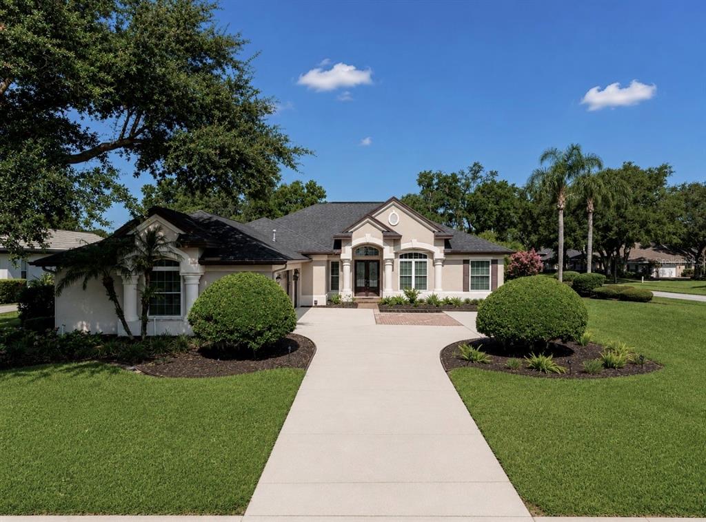 A single-story house with a concrete driveway, manicured lawn, and two large round bushes — 6105 AUDUBON MANOR BOULEVARD, LITHIA, FL