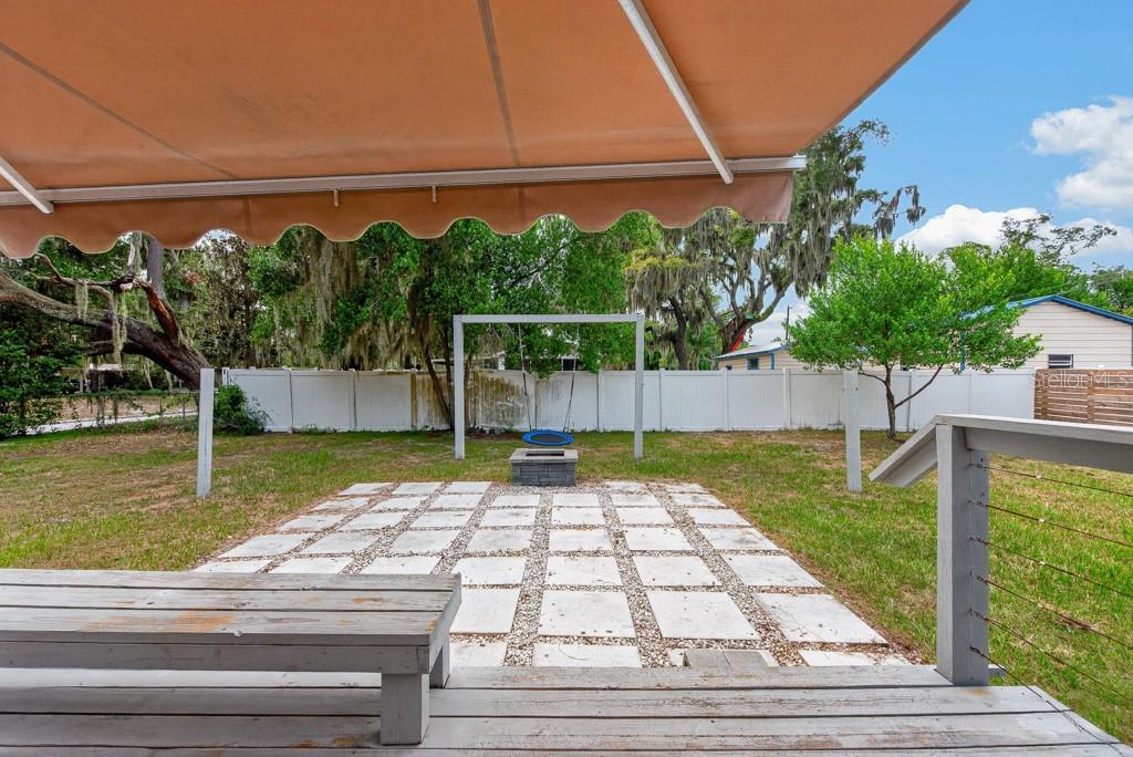 A backyard features a wooden deck with a bench, a paved patio, and a swing set — 215 S ELM ROAD, LAKELAND, FL