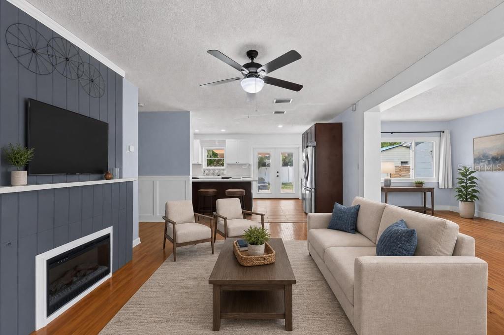 A living room with a fireplace, gray accent wall, ceiling fan, and open kitchen view — 215 S ELM ROAD, LAKELAND, FL