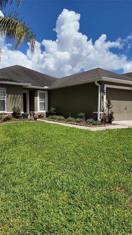 A single-story house with olive green stucco walls, a tan garage door, and a grassy lawn — 1870 RUFUS KING DRIVE, ST CLOUD, FL