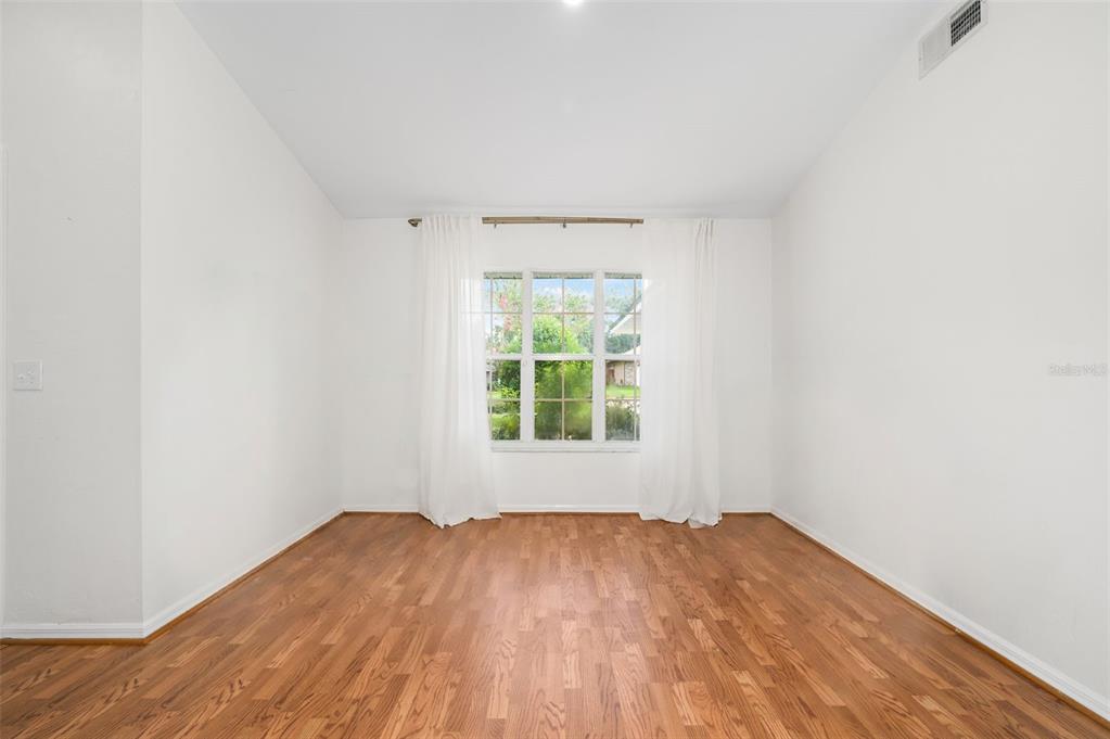 An empty room with white walls, hardwood floors, and a window with white curtains — 10001 NW 12TH LANE, GAINESVILLE, FL
