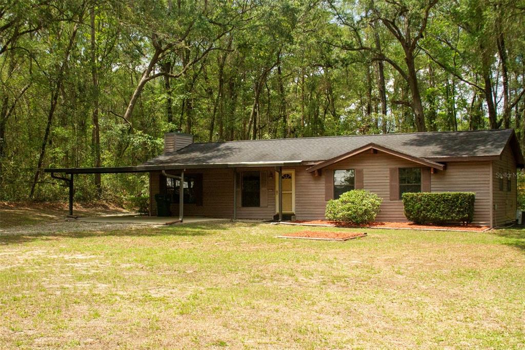 A single-story house with brown siding, a dark shingled roof, and an attached carport — 16326 NW 118TH PLACE, ALACHUA, FL