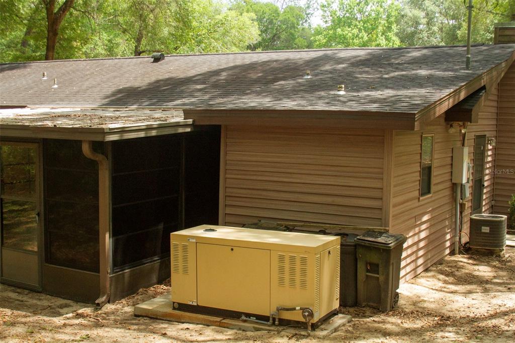 A tan standby generator sits on a concrete pad outside a house with brown siding — 16326 NW 118TH PLACE, ALACHUA, FL