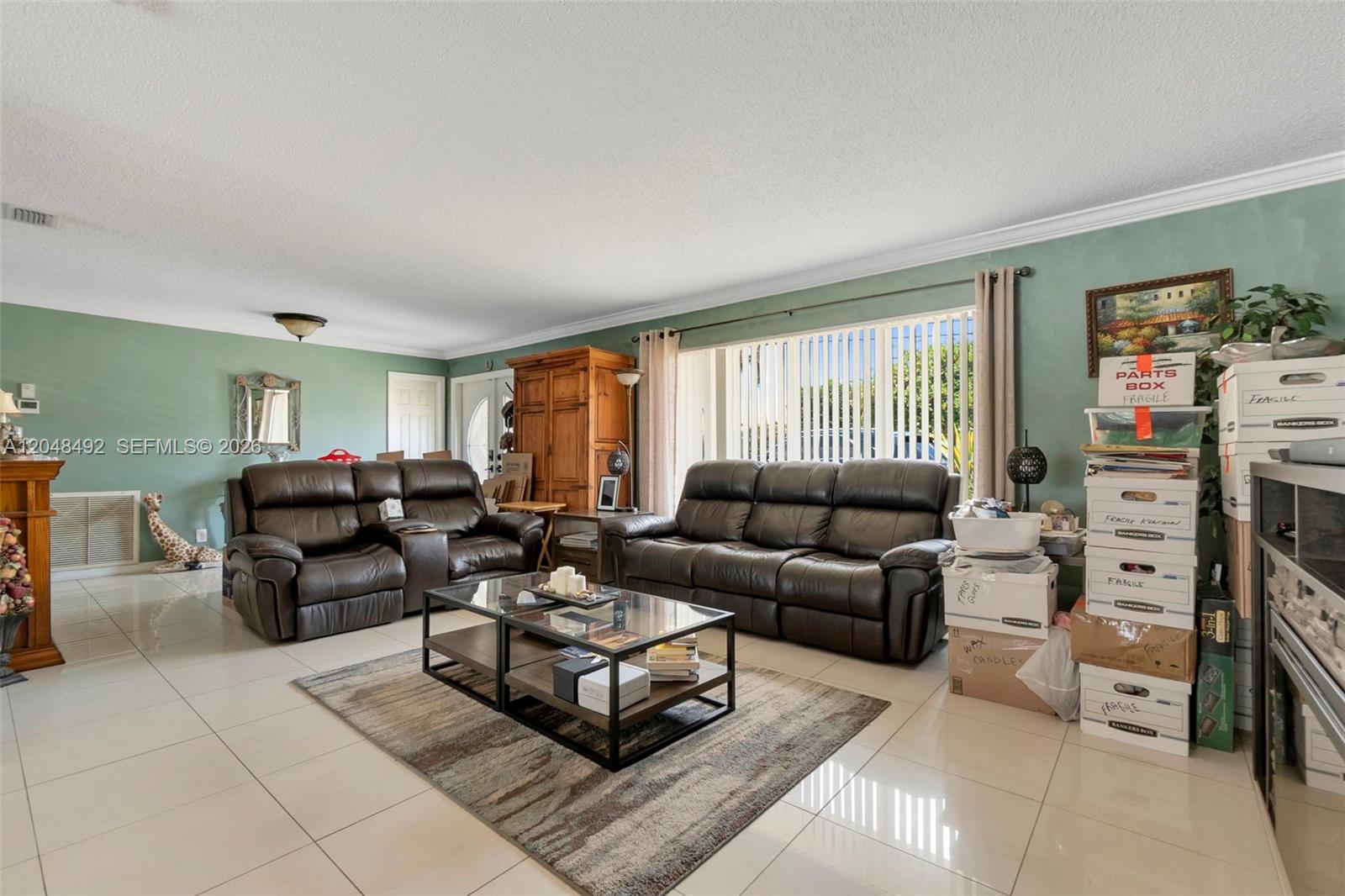 A living room with light tile floors, two brown leather sofas, and stacked storage boxes — 2480 NE 46th St, Lighthouse Point FL 33064, LIGHTHOUSE POINT, FL