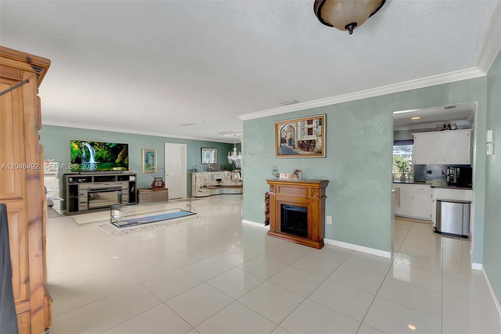 A spacious living room features light green walls, white tile floors, and a wood fireplace — 2480 NE 46th St, Lighthouse Point FL 33064, LIGHTHOUSE POINT, FL