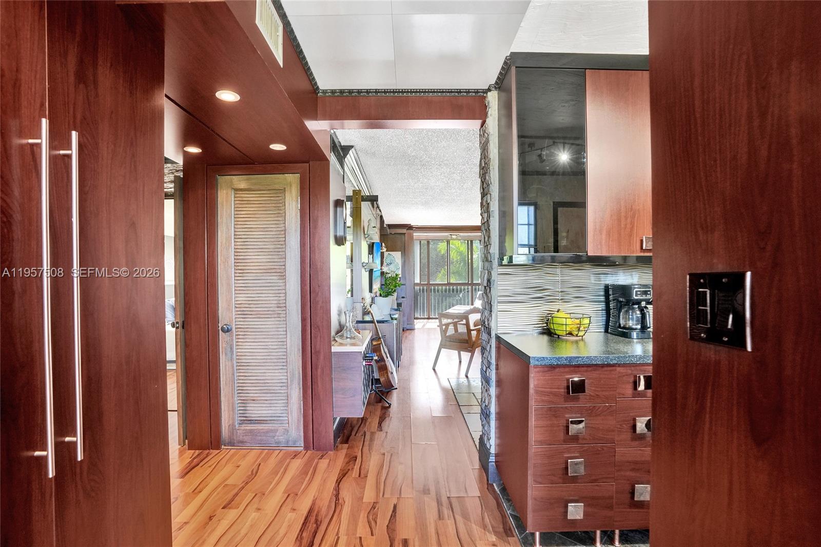 A hallway with wood flooring leads to a kitchen featuring dark cabinetry and stone accents — 1000 NE 12th Ave # 505, Hallandale Beach FL 33009, HALLANDALE BEACH, FL