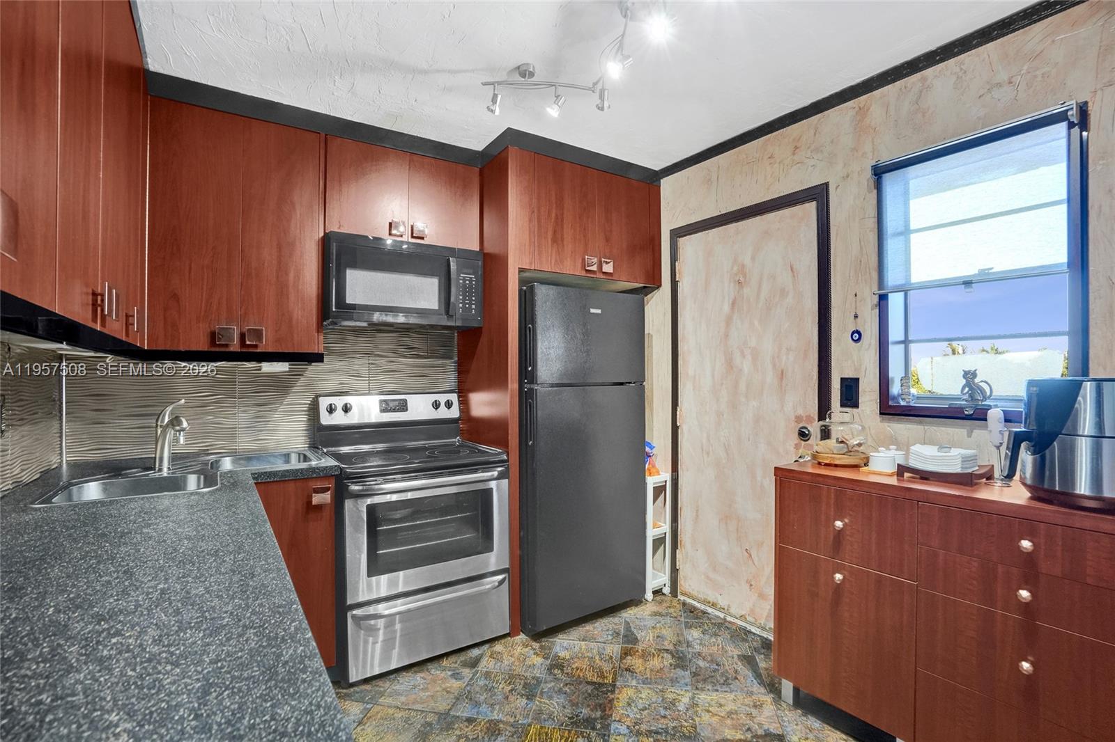 A kitchen features cherry-toned cabinets, black appliances, a textured backsplash, and dark stone countertops — 1000 NE 12th Ave # 505, Hallandale Beach FL 33009, HALLANDALE BEACH, FL