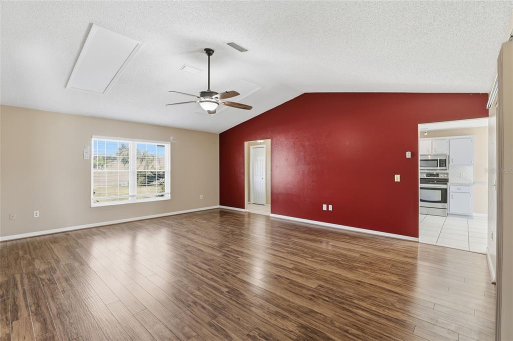 An empty living room features wood-look flooring, a vaulted ceiling, and a red accent wall — 3940 SW 134TH STREET, OCALA, FL